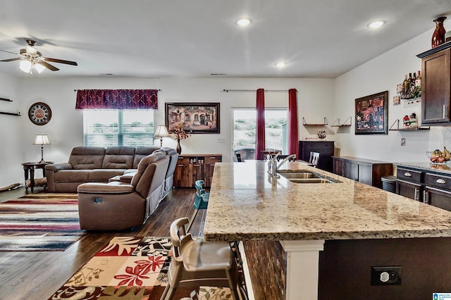 kitchen featuring a center island with sink, sink, light stone countertops, dark hardwood / wood-style flooring, and dark brown cabinetry