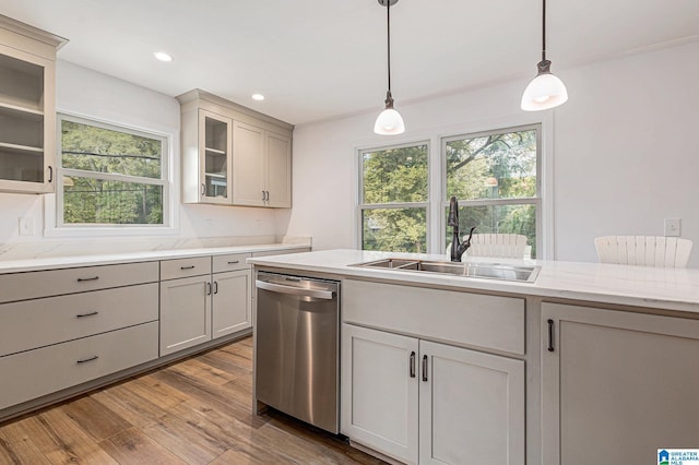 kitchen with sink, hanging light fixtures, light stone counters, light hardwood / wood-style flooring, and stainless steel dishwasher