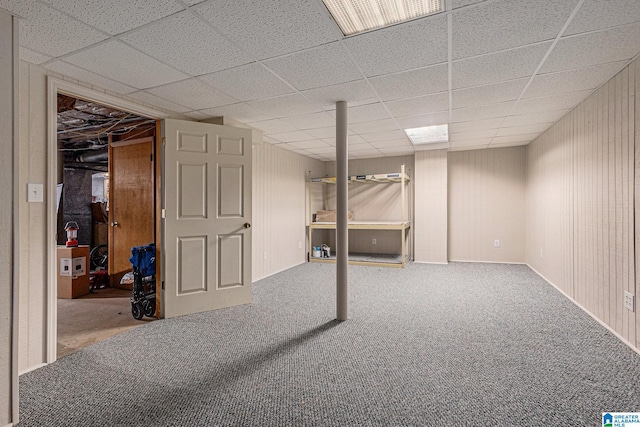 basement with carpet flooring, a paneled ceiling, and wood walls