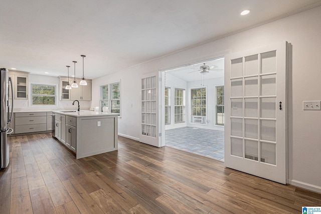 kitchen with stainless steel refrigerator, sink, hanging light fixtures, dark hardwood / wood-style floors, and an island with sink