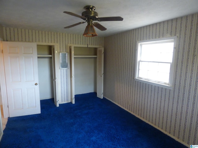 unfurnished bedroom featuring dark colored carpet, ceiling fan, and two closets