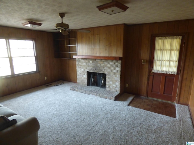 unfurnished living room featuring carpet, ceiling fan, wooden walls, and a brick fireplace