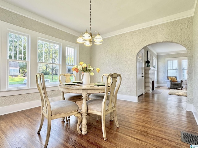 dining space with hardwood / wood-style flooring, crown molding, a fireplace, and an inviting chandelier