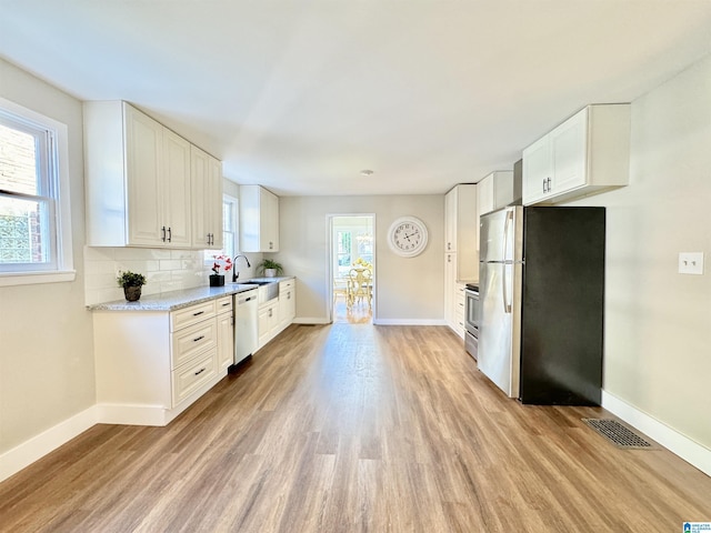 kitchen featuring white cabinets, light wood-type flooring, stainless steel appliances, and a wealth of natural light