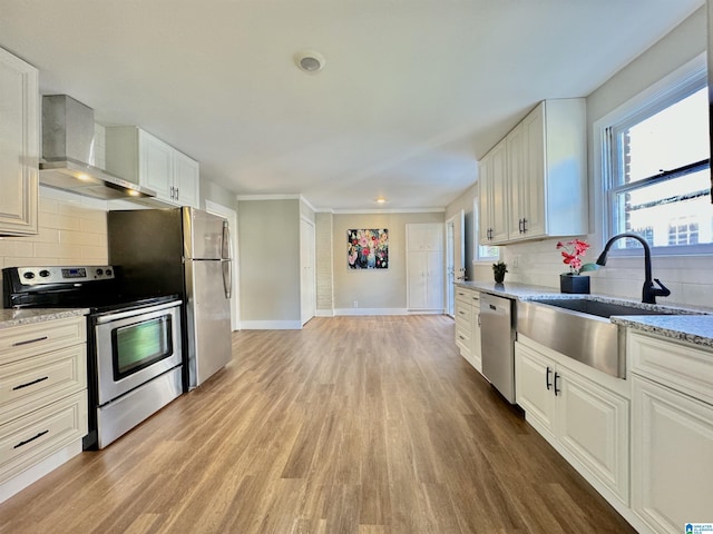 kitchen featuring appliances with stainless steel finishes, wall chimney exhaust hood, sink, light hardwood / wood-style flooring, and white cabinets