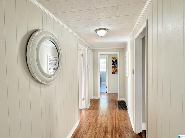 hallway featuring wood-type flooring, crown molding, and wooden walls