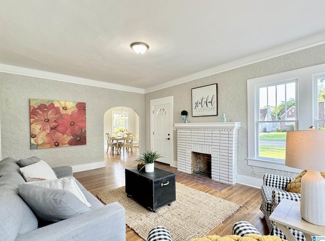 living room featuring wood-type flooring, a brick fireplace, and ornamental molding