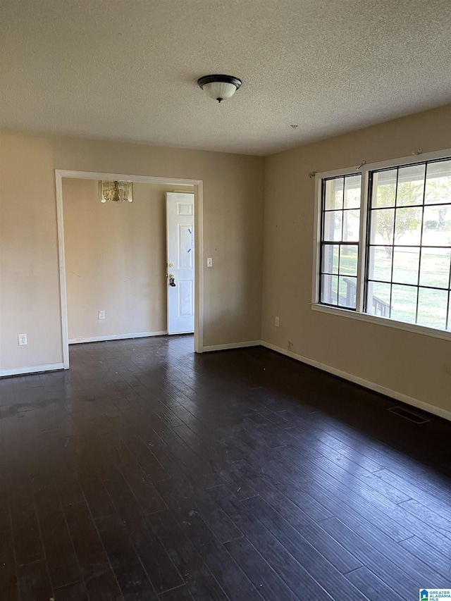 unfurnished room featuring a textured ceiling, dark hardwood / wood-style floors, and an inviting chandelier