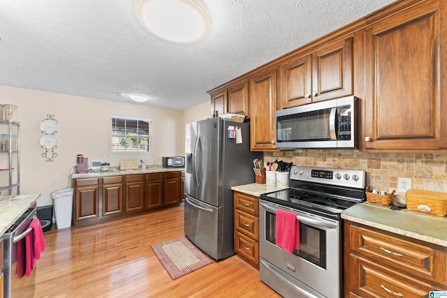 kitchen featuring decorative backsplash, a textured ceiling, appliances with stainless steel finishes, and light hardwood / wood-style flooring