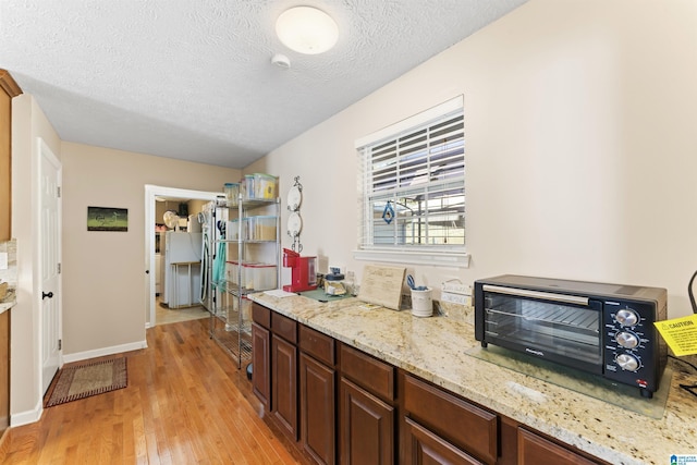 kitchen featuring a textured ceiling, light hardwood / wood-style flooring, and light stone counters