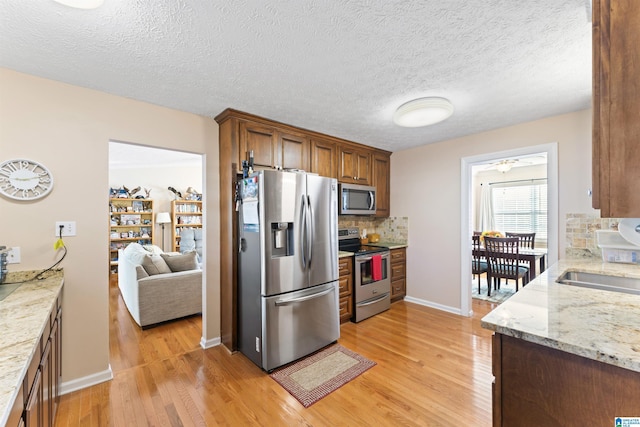 kitchen featuring light hardwood / wood-style flooring, decorative backsplash, a textured ceiling, light stone counters, and stainless steel appliances