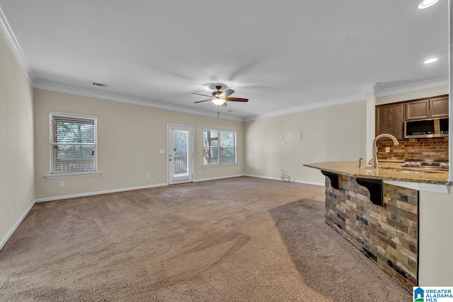 unfurnished living room featuring a healthy amount of sunlight, ornamental molding, and light carpet