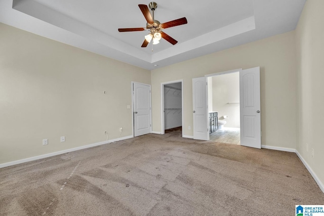 unfurnished bedroom featuring carpet floors, a tray ceiling, a spacious closet, and ceiling fan