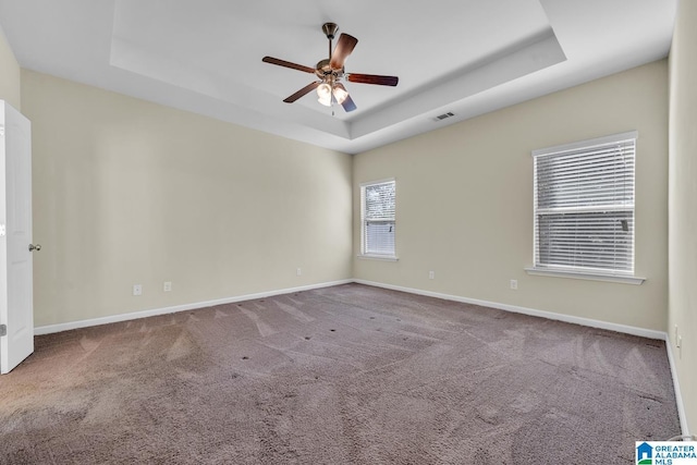 empty room with ceiling fan, a raised ceiling, and carpet floors