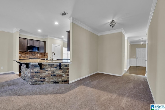 kitchen with tasteful backsplash, dark brown cabinets, crown molding, carpet floors, and a breakfast bar area