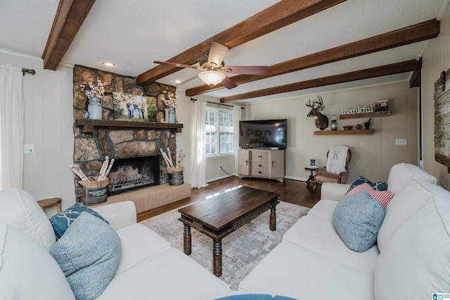 living room with ceiling fan, a stone fireplace, beamed ceiling, a textured ceiling, and hardwood / wood-style flooring