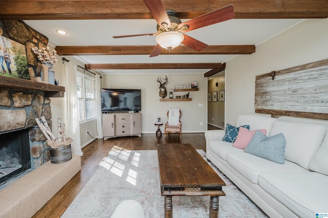 living room with beamed ceiling, a stone fireplace, ceiling fan, and dark wood-type flooring