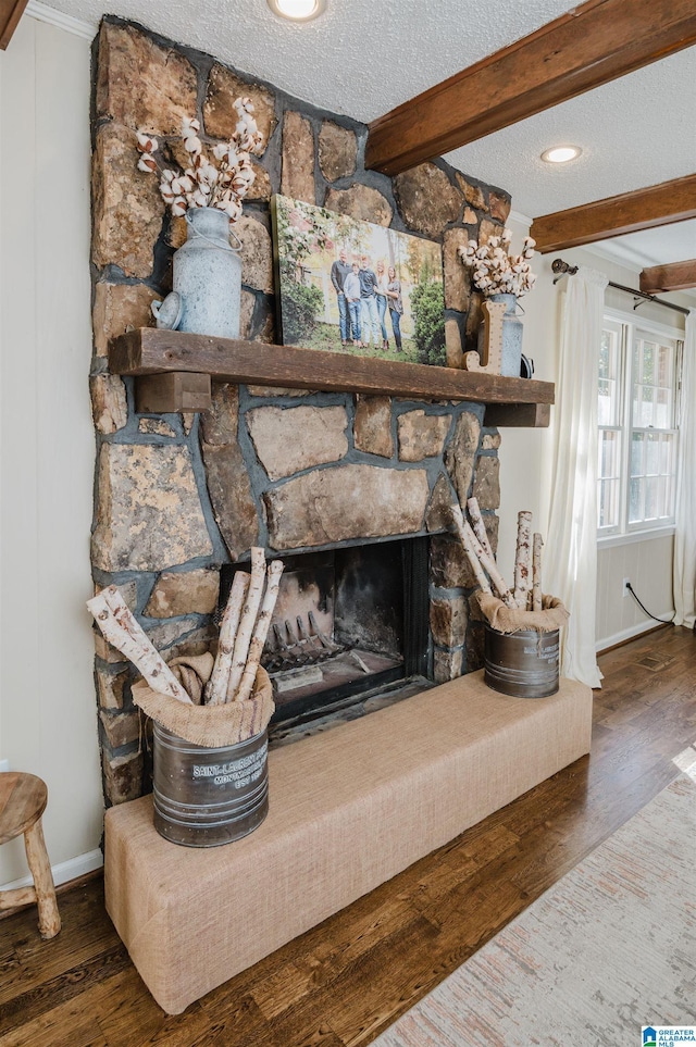 details with hardwood / wood-style flooring, beam ceiling, a stone fireplace, and a textured ceiling