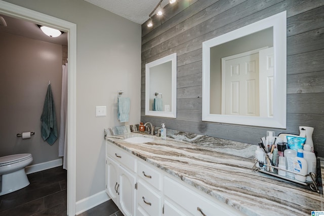 bathroom with vanity, wood walls, tile patterned floors, toilet, and a textured ceiling