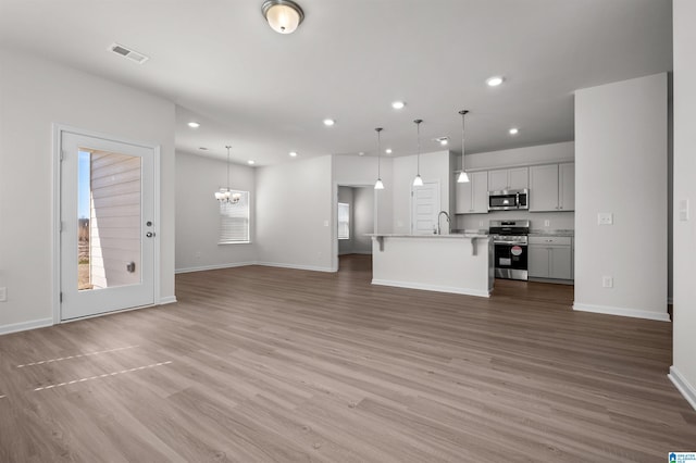 unfurnished living room with sink, an inviting chandelier, and light hardwood / wood-style flooring