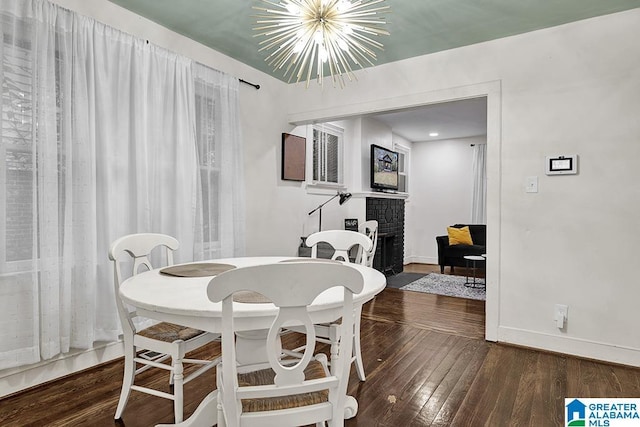 dining area with a brick fireplace, dark hardwood / wood-style flooring, and a notable chandelier