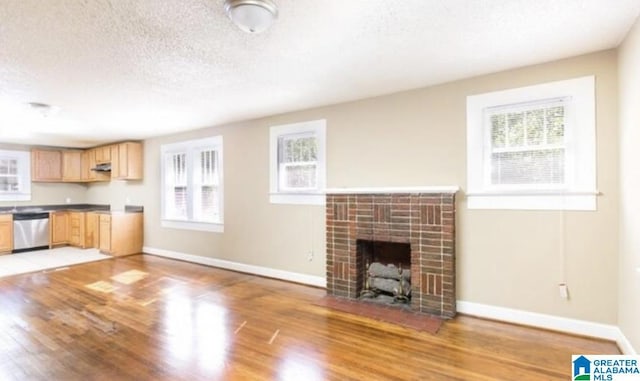 unfurnished living room with baseboards, a textured ceiling, a fireplace, and light wood finished floors