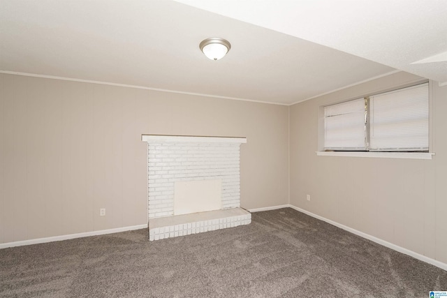 empty room with a fireplace, dark carpet, and crown molding