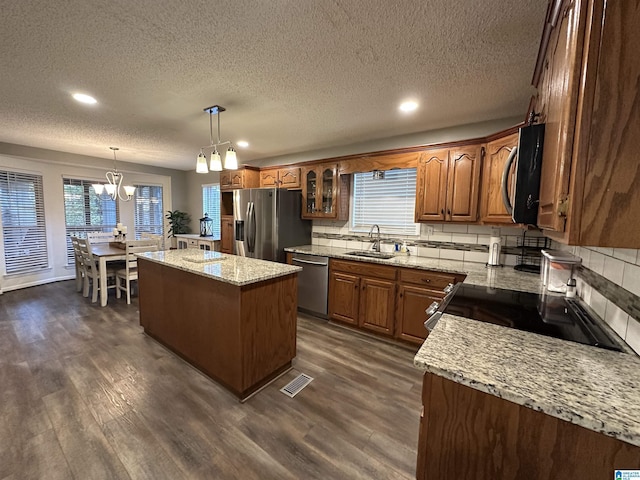 kitchen featuring appliances with stainless steel finishes, tasteful backsplash, dark wood-type flooring, decorative light fixtures, and a kitchen island