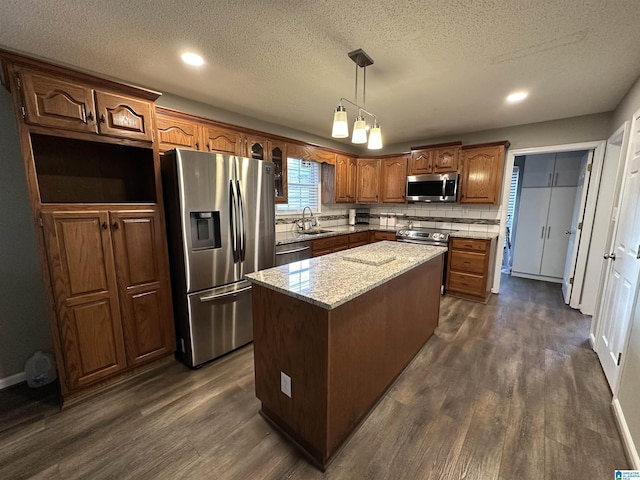 kitchen with appliances with stainless steel finishes, dark hardwood / wood-style flooring, sink, a center island, and hanging light fixtures