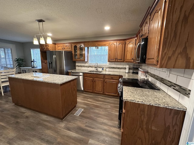 kitchen featuring appliances with stainless steel finishes, dark wood-type flooring, sink, decorative light fixtures, and a kitchen island