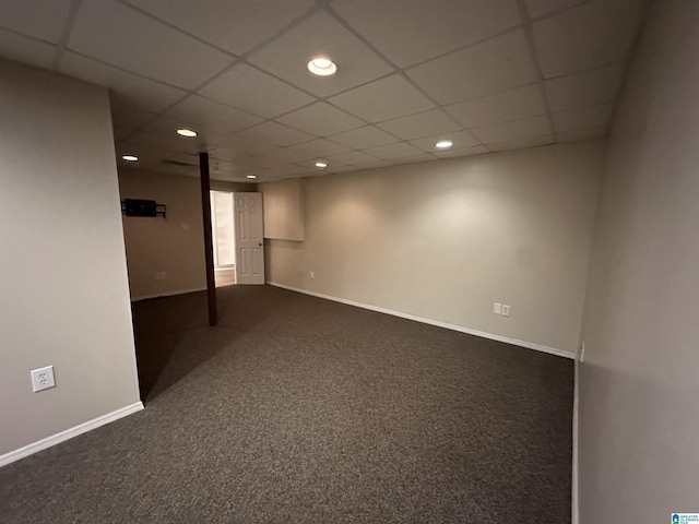 basement with a paneled ceiling and dark colored carpet