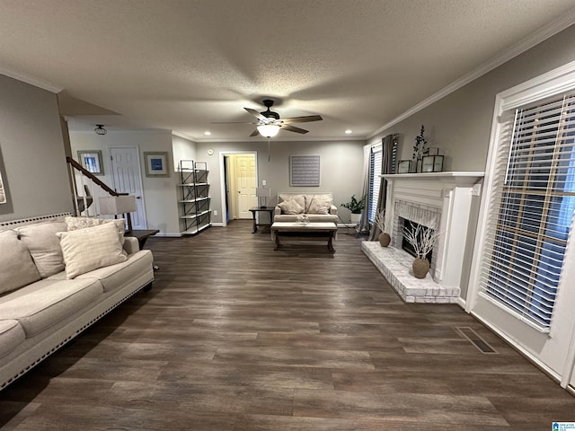 living room featuring a brick fireplace, a textured ceiling, ceiling fan, crown molding, and dark hardwood / wood-style floors