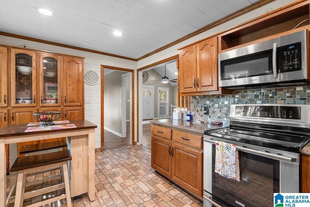 kitchen with ornamental molding, stainless steel appliances, tasteful backsplash, and dark stone counters