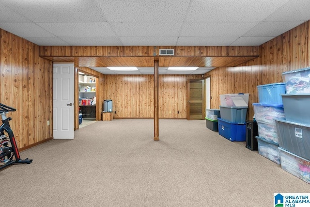 basement with carpet floors, a drop ceiling, and wooden walls