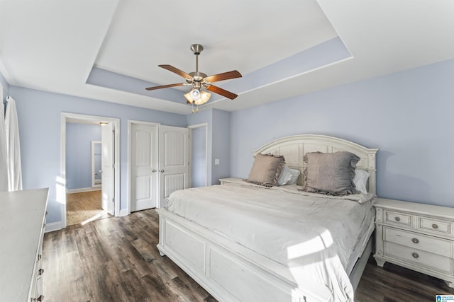 bedroom featuring connected bathroom, dark hardwood / wood-style floors, a raised ceiling, and ceiling fan