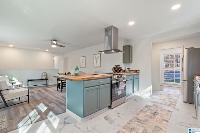 kitchen with ceiling fan, wall chimney range hood, butcher block countertops, light hardwood / wood-style floors, and appliances with stainless steel finishes