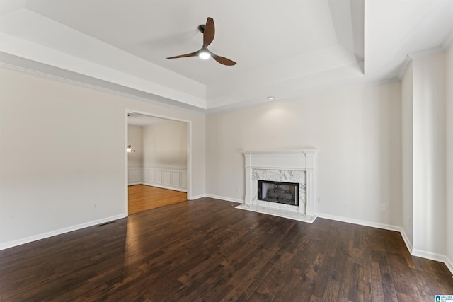 unfurnished living room featuring a high end fireplace, dark hardwood / wood-style flooring, a raised ceiling, and ceiling fan