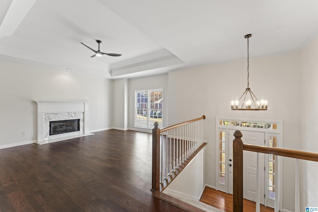 interior space with wood-type flooring, ceiling fan with notable chandelier, a raised ceiling, and a premium fireplace