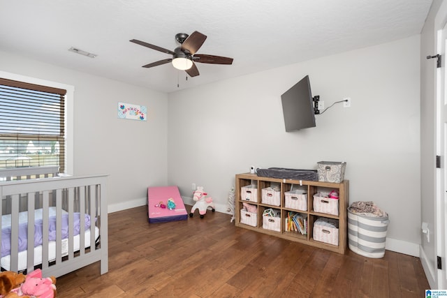 bedroom featuring a crib, dark hardwood / wood-style flooring, and ceiling fan