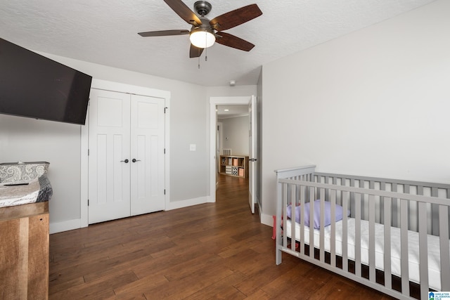 bedroom featuring ceiling fan, dark hardwood / wood-style flooring, a textured ceiling, a closet, and a nursery area