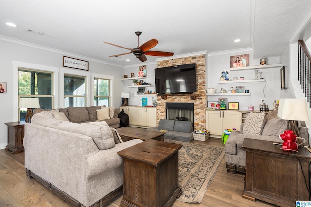 living room with light hardwood / wood-style floors, a stone fireplace, ceiling fan, and crown molding