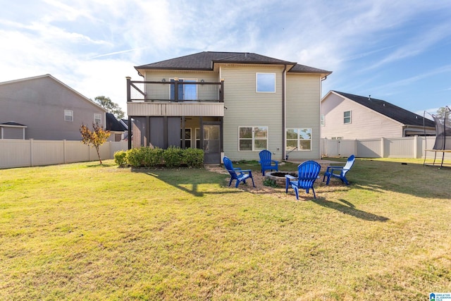 back of property featuring a trampoline, a balcony, an outdoor fire pit, and a lawn