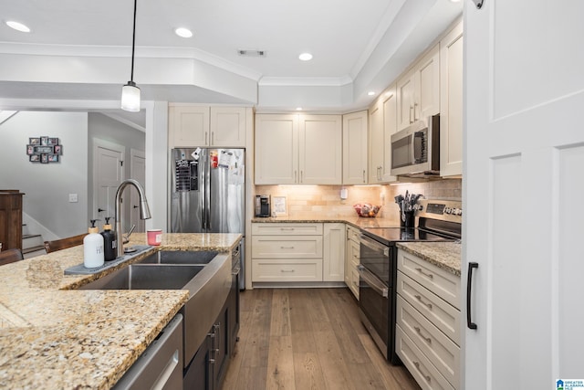 kitchen with crown molding, hanging light fixtures, light stone countertops, wood-type flooring, and stainless steel appliances