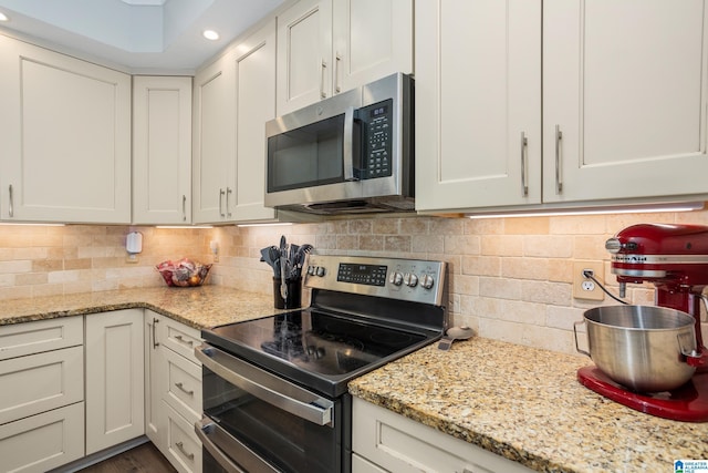 kitchen with white cabinets, light stone countertops, stainless steel appliances, and tasteful backsplash