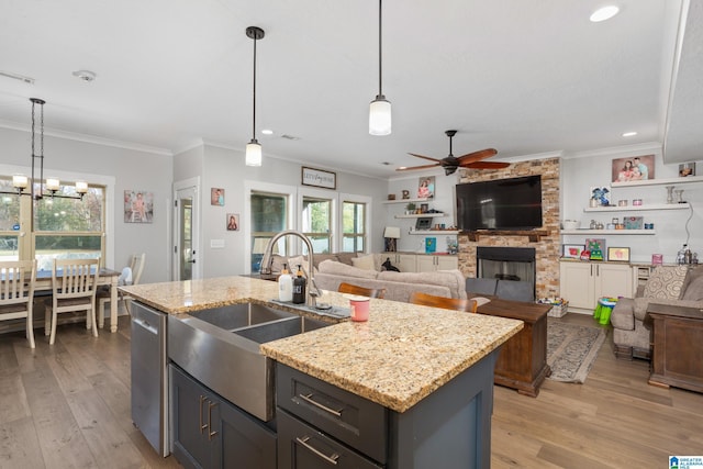 kitchen featuring pendant lighting, a center island with sink, ceiling fan with notable chandelier, a fireplace, and light hardwood / wood-style floors