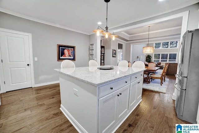 kitchen featuring white cabinetry, stainless steel fridge, wood-type flooring, decorative light fixtures, and a kitchen island