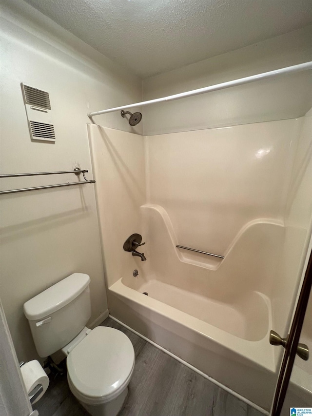 bathroom with toilet, wood-type flooring, a textured ceiling, and bathtub / shower combination