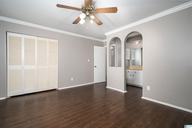 unfurnished bedroom featuring dark wood-type flooring, crown molding, ensuite bath, ceiling fan, and a closet