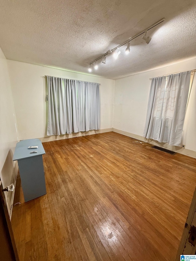 empty room featuring wood-type flooring, a textured ceiling, and track lighting