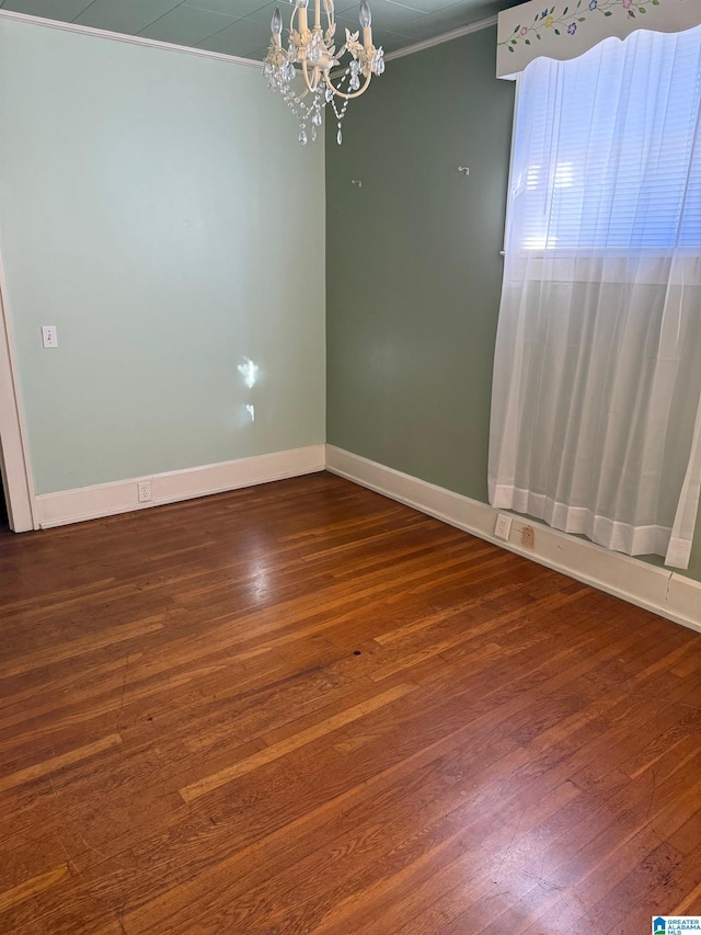 empty room featuring a chandelier, ornamental molding, and dark wood-type flooring